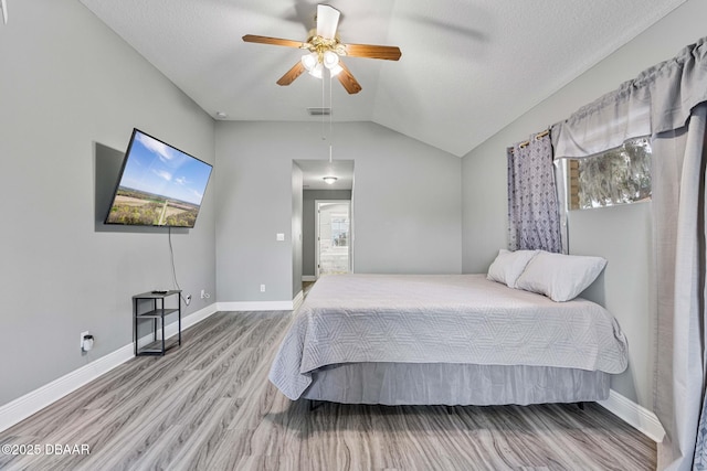 bedroom with ceiling fan, lofted ceiling, wood-type flooring, and a textured ceiling