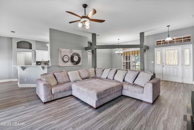 living room with lofted ceiling, ceiling fan with notable chandelier, and light wood-type flooring