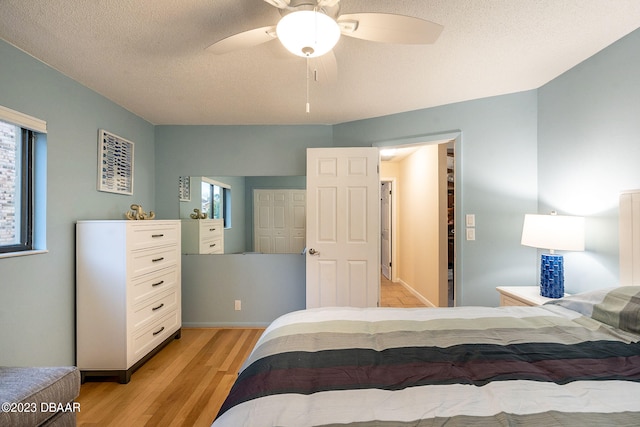 bedroom with a textured ceiling, light hardwood / wood-style floors, multiple windows, and ceiling fan