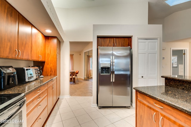 kitchen with dark stone counters, stainless steel fridge with ice dispenser, light tile patterned floors, and lofted ceiling with skylight