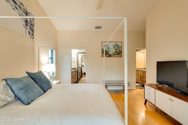 bedroom with ensuite bathroom, a towering ceiling, ceiling fan, and light hardwood / wood-style flooring