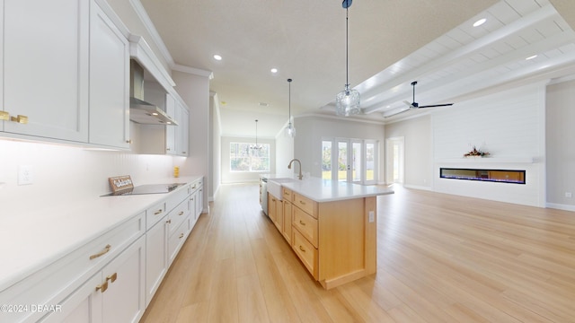 kitchen with pendant lighting, white cabinets, beam ceiling, an island with sink, and light hardwood / wood-style floors