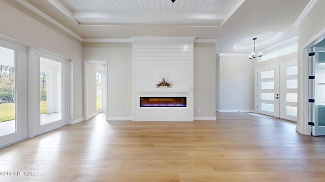 unfurnished living room with an inviting chandelier, french doors, light hardwood / wood-style flooring, a tray ceiling, and a large fireplace