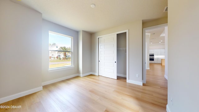 unfurnished bedroom featuring light hardwood / wood-style floors, a textured ceiling, and a closet