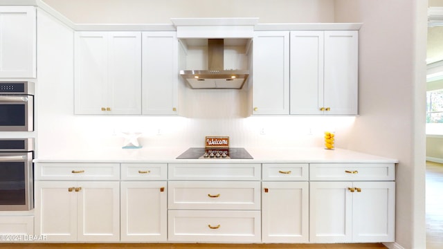 kitchen with black electric stovetop, white cabinetry, double oven, and wall chimney exhaust hood