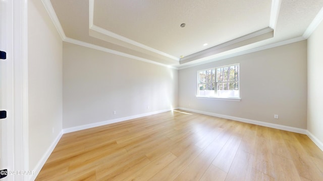 spare room featuring a tray ceiling, light hardwood / wood-style flooring, and crown molding