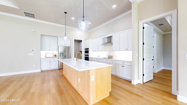 kitchen with white cabinetry, wall chimney range hood, a center island with sink, appliances with stainless steel finishes, and light wood-type flooring