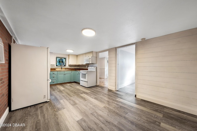 kitchen with wood walls, white appliances, sink, green cabinetry, and light hardwood / wood-style floors