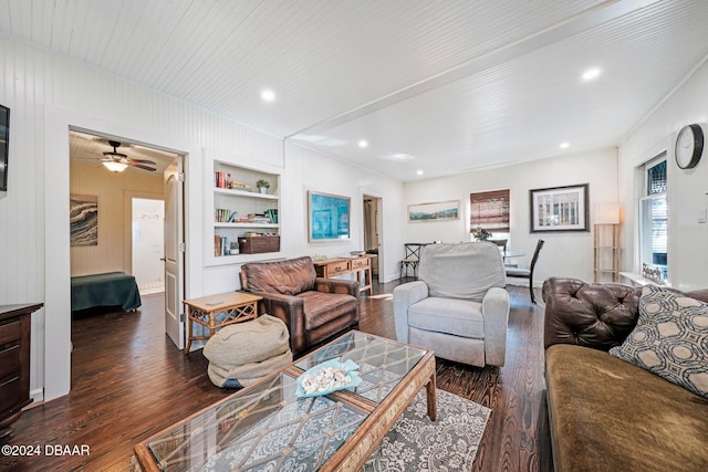 living room with built in shelves, ceiling fan, dark wood-type flooring, and wood walls