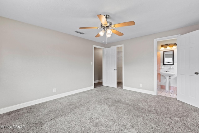 unfurnished bedroom with ceiling fan, a walk in closet, carpet floors, and connected bathroom