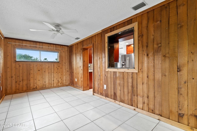 unfurnished room with a textured ceiling, ceiling fan, wood walls, visible vents, and baseboards