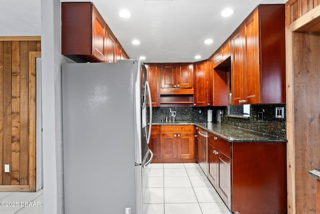 kitchen with light tile patterned floors, tasteful backsplash, appliances with stainless steel finishes, a sink, and dark stone countertops