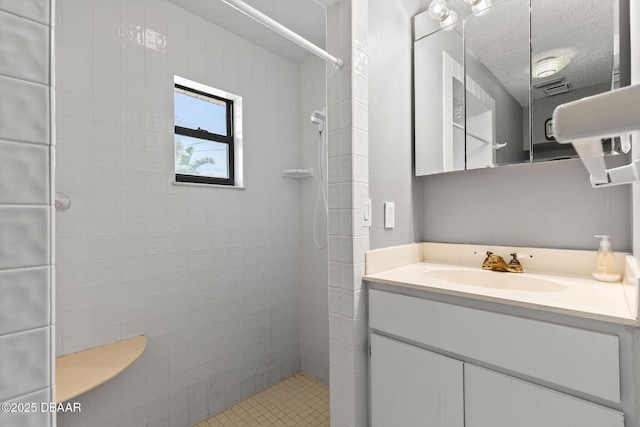 bathroom featuring a textured ceiling, tiled shower, and vanity