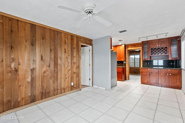 kitchen featuring light tile patterned floors, glass insert cabinets, freestanding refrigerator, wood walls, and backsplash