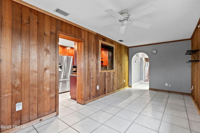 unfurnished room with arched walkways, a ceiling fan, visible vents, and wooden walls