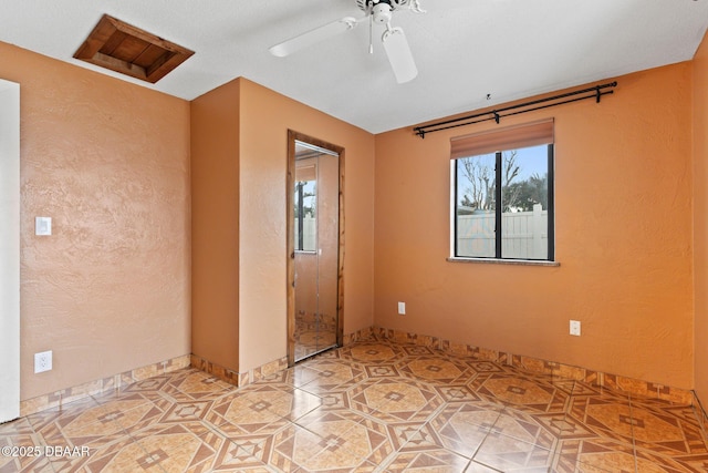 empty room with light tile patterned floors, a textured wall, attic access, and a ceiling fan