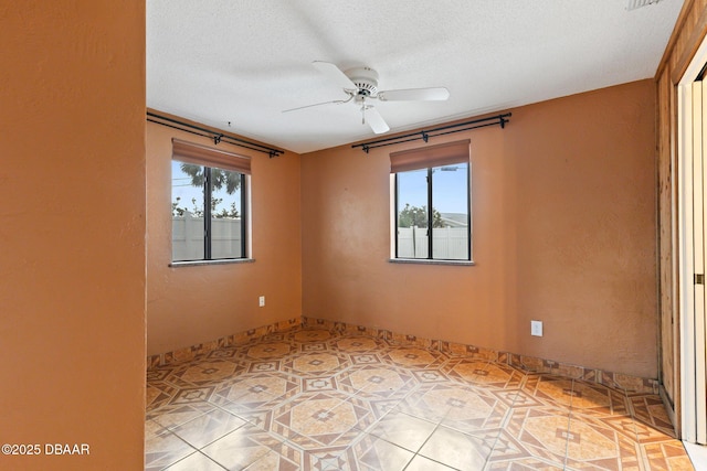 empty room featuring a wealth of natural light, ceiling fan, and a textured ceiling