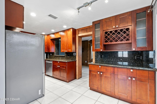 kitchen with appliances with stainless steel finishes, light tile patterned floors, glass insert cabinets, and tasteful backsplash