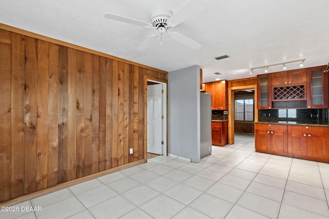 kitchen with wooden walls, glass insert cabinets, freestanding refrigerator, backsplash, and light tile patterned flooring