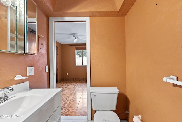 bathroom with a textured wall, toilet, ceiling fan, vanity, and tile patterned flooring