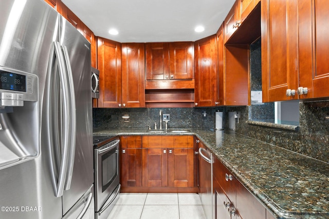 kitchen with light tile patterned floors, appliances with stainless steel finishes, dark stone countertops, a sink, and backsplash