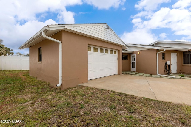 view of property exterior featuring a yard, stucco siding, an attached garage, fence, and driveway