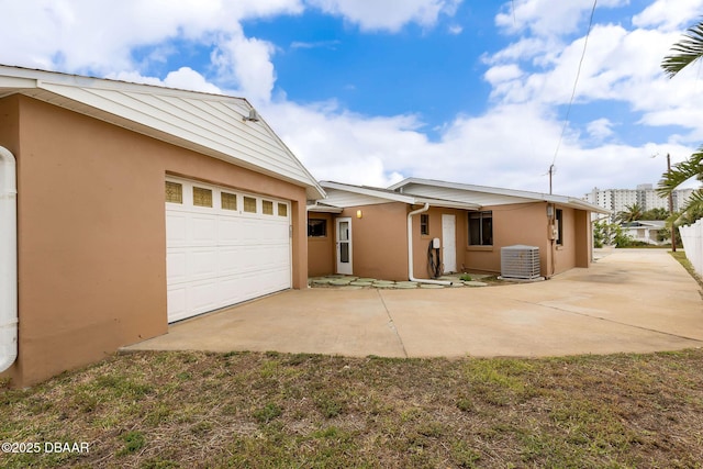 view of front of home featuring a garage, central air condition unit, concrete driveway, and stucco siding