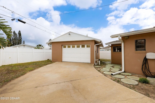 detached garage featuring concrete driveway and fence