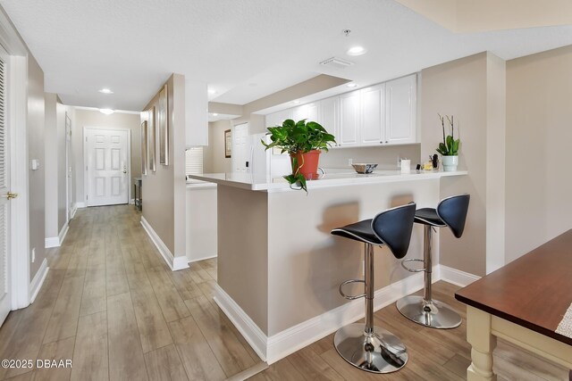 4670 Links Village Dr Unit A506, Ponce Inlet, FL 32127 - kitchen with light countertops, white cabinetry, light wood finished floors, and a kitchen bar