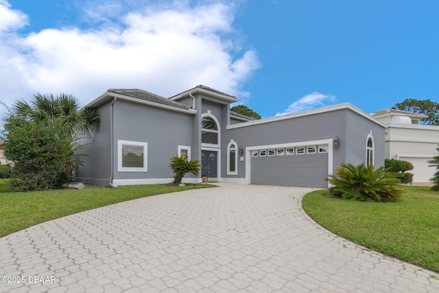 view of front of house with curved driveway, a garage, a front lawn, and stucco siding