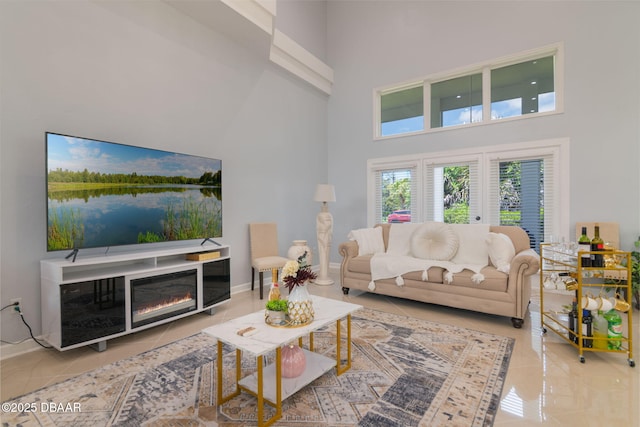 living room with baseboards, a glass covered fireplace, tile patterned flooring, and a towering ceiling