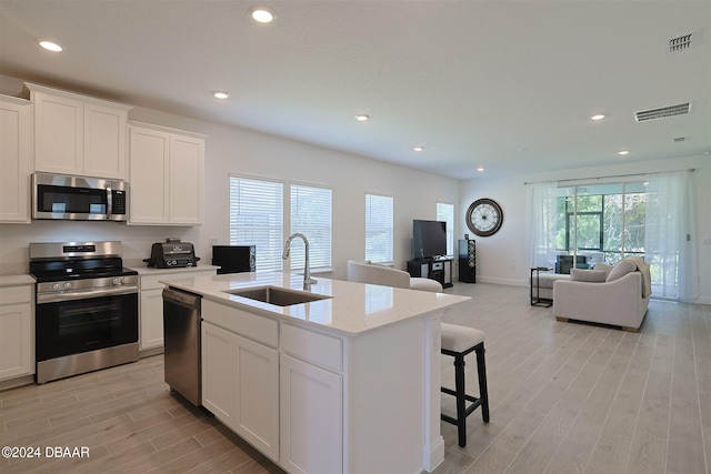 kitchen with white cabinetry, sink, appliances with stainless steel finishes, a kitchen island with sink, and light hardwood / wood-style flooring