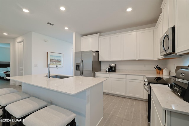 kitchen with stainless steel appliances, white cabinetry, sink, and a kitchen island with sink