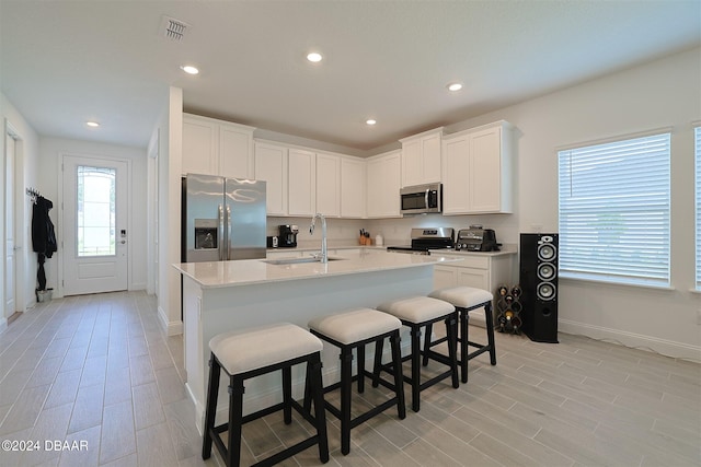 kitchen with a center island with sink, light hardwood / wood-style flooring, sink, white cabinetry, and appliances with stainless steel finishes