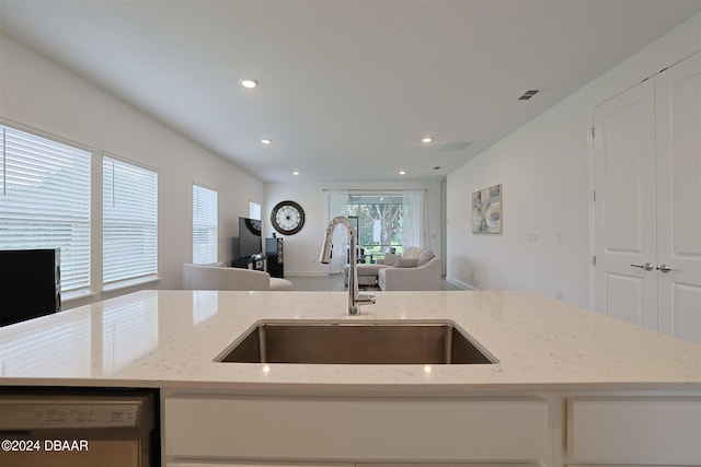 kitchen featuring light stone countertops, sink, an island with sink, and white dishwasher