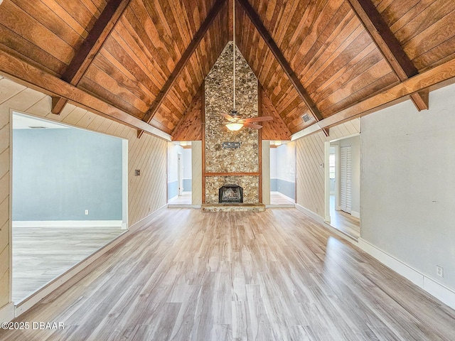 unfurnished living room with beamed ceiling, a stone fireplace, light hardwood / wood-style floors, and wooden ceiling