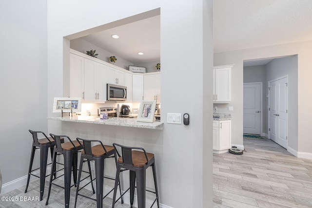 3417 Medici Blvd, New Smyrna Beach, FL 32168 - kitchen with stainless steel appliances, light wood-style floors, a breakfast bar, white cabinetry, and light stone countertops