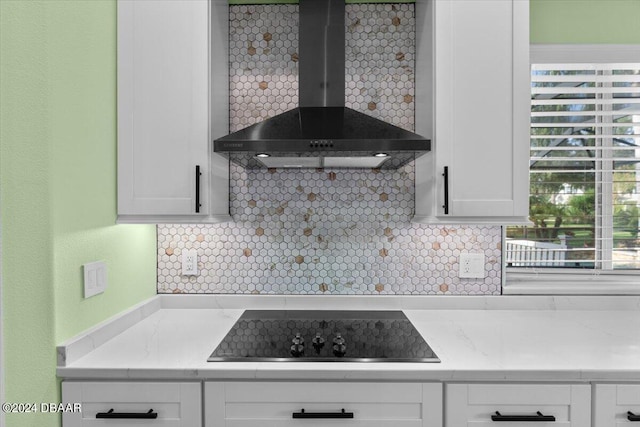 kitchen featuring wall chimney range hood, decorative backsplash, and white cabinets