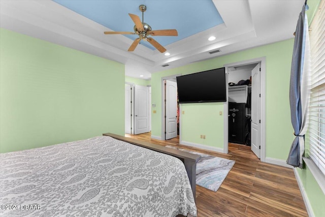 bedroom featuring a closet, a walk in closet, dark hardwood / wood-style floors, a tray ceiling, and ceiling fan