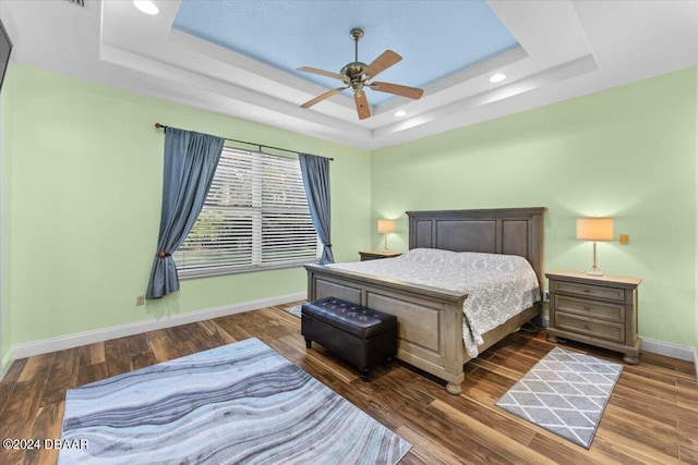 bedroom with ceiling fan, a tray ceiling, and dark hardwood / wood-style floors