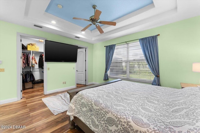 bedroom with a closet, a spacious closet, wood-type flooring, a raised ceiling, and ceiling fan