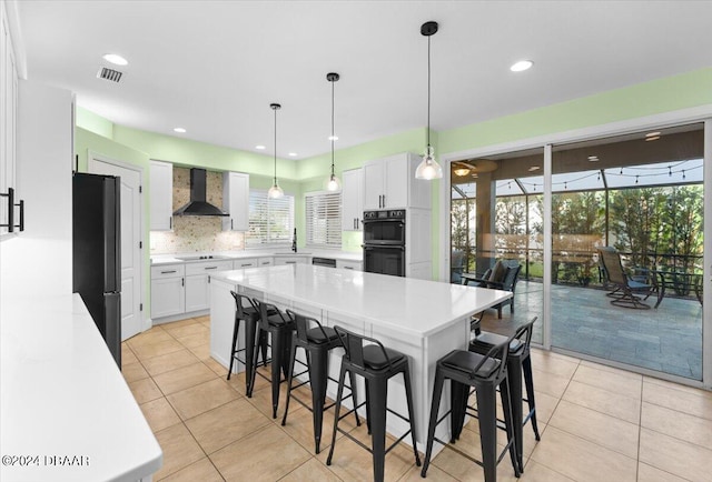 kitchen featuring white cabinets, wall chimney range hood, pendant lighting, and black appliances