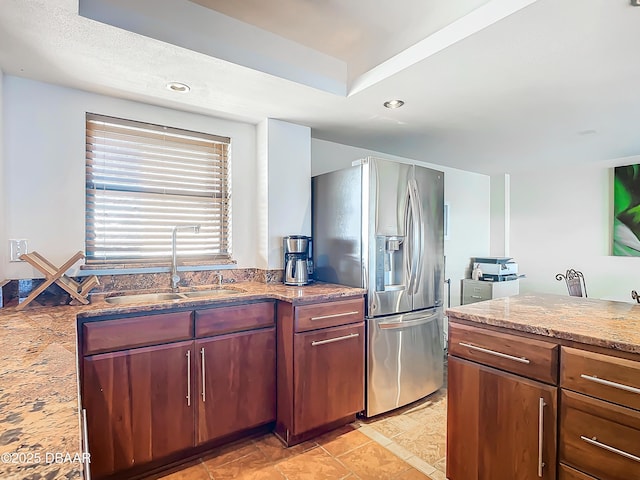 kitchen featuring stainless steel refrigerator with ice dispenser, sink, and light stone counters