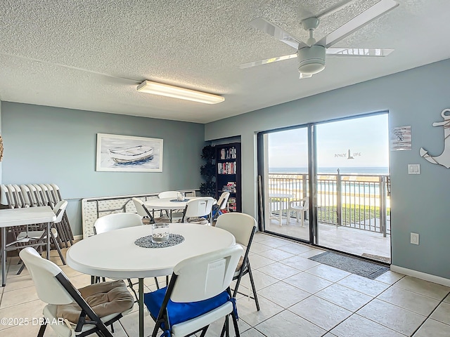 dining room featuring light tile patterned flooring, a water view, a textured ceiling, and ceiling fan