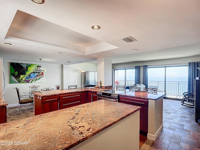 kitchen with light stone countertops, a raised ceiling, kitchen peninsula, and a kitchen island