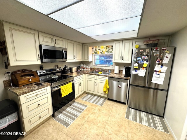 kitchen featuring cream cabinetry, light tile patterned floors, stainless steel appliances, a sink, and baseboards