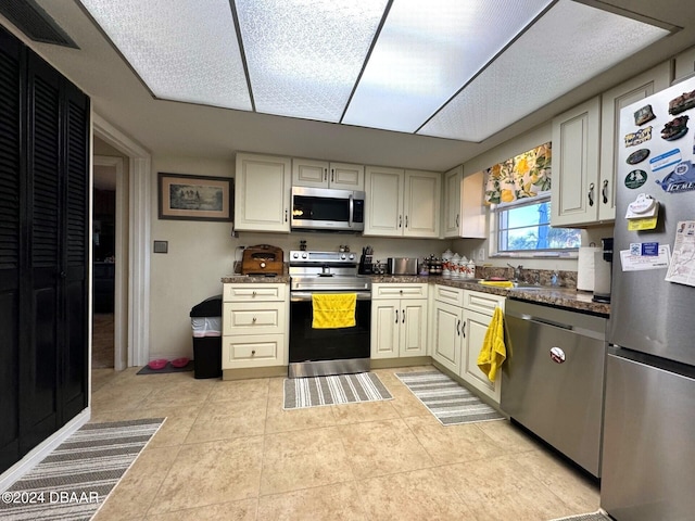 kitchen featuring light tile patterned floors, visible vents, dark countertops, appliances with stainless steel finishes, and a sink