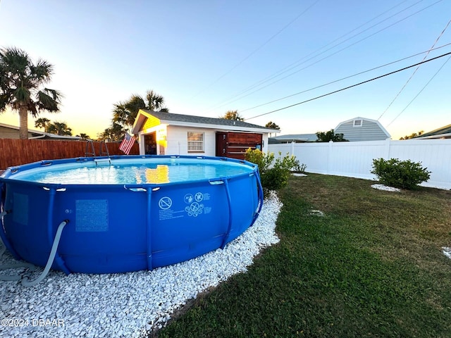 pool at dusk with a yard, a fenced backyard, and a fenced in pool