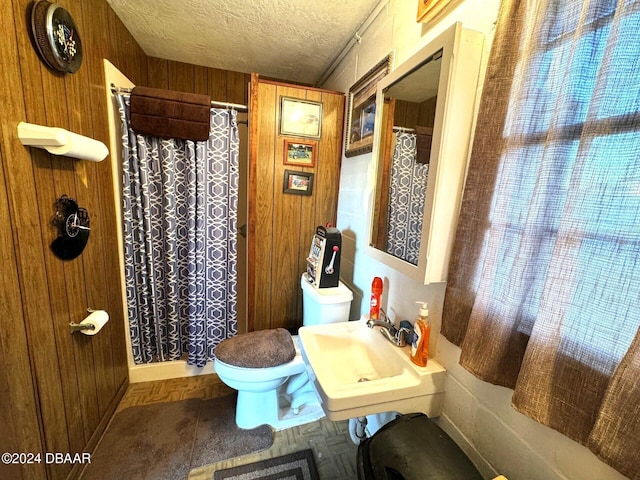 bathroom featuring a textured ceiling, curtained shower, toilet, wood walls, and a sink