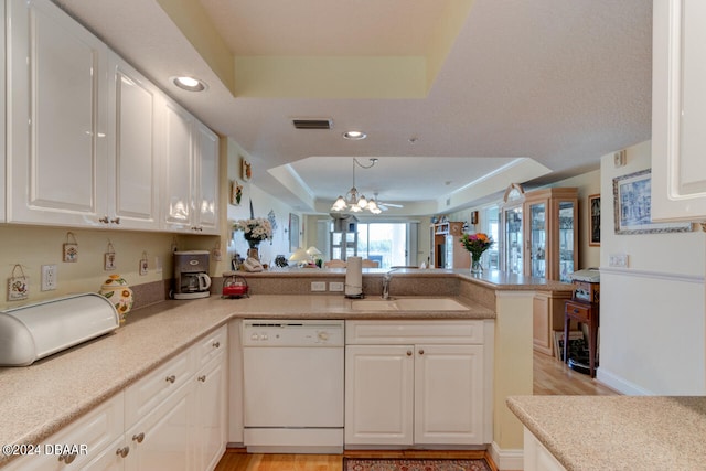 kitchen with dishwasher, kitchen peninsula, white cabinets, hanging light fixtures, and a raised ceiling